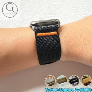 May include: A black elastic watch band featuring a single horizontal orange stitched line, attached to a metallic watch casing. The band has a textured fabric surface. Four small circular icons display various metallic and patterned buckle options.