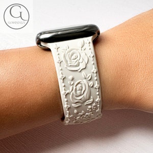 May include: White silicone Apple Watch band with a raised floral design. The band features three roses and leaves.
