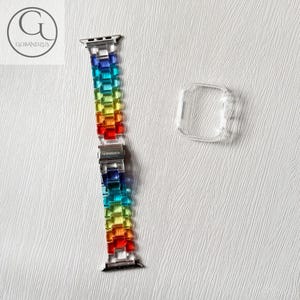 May include: A rainbow-colored link watch band made of translucent resin segments with a silver-toned metal clasp featuring the text GOBANDZUS, accompanied by a separate clear, rectangular protective watch case cover for a digital timepiece.