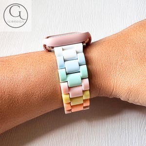 Pode incluir: Uma pulseira de relógio arco-íris pastel com caixa branca e mostrador rosa. A pulseira é feita de silicone e tem um design de elo.