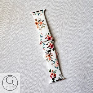 May include: White silicone Apple Watch band with a floral print featuring pink, red, and orange flowers. The band has a white background with green leaves.