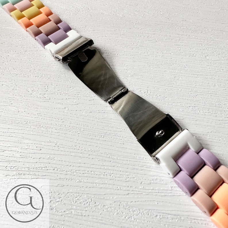 Op de afbeelding: Een kleurrijk pastelkleurig horlogebandje met een zilveren metalen sluiting. Het bandje is gemaakt van siliconen en heeft een regenboogkleurenpatroon.
