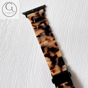 May include: A tortoiseshell patterned Apple Watch band with a black metal clasp.