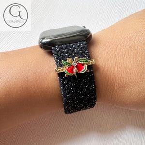 Puede incluir: Pulsera de reloj con estampado en blanco y negro con un dije de lazo de Navidad dorado y rojo.
