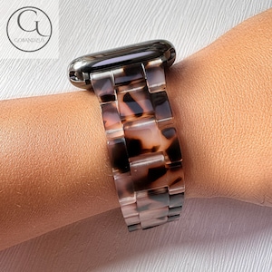 May include: A brown and black tortoise shell patterned watch band with a silver watch face.