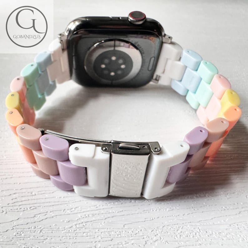 Op de afbeelding: Een wit en pastel regenboogkleurig Apple Watch-bandje met een witte sluiting. Het bandje is gemaakt van siliconen en heeft een gladde afwerking.