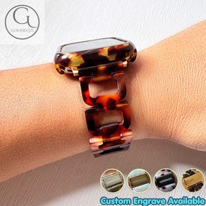Op de afbeelding: Een smartwatchband met een bruin en zwart schildpadpatroon en in elkaar grijpende rechthoekige schakels. De band is verbonden met een bijpassende horlogekast. Vier kleine ronde iconen tonen metalen sluitingen met de tekst GOBANDZUS.