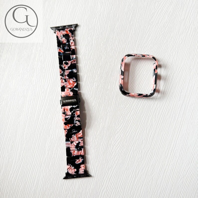 Puede incluir: Una correa de reloj y una funda protectora rectangular a juego, ambas con un patr&oacute;n de m&aacute;rmol en negro, blanco y rosa suave. La correa incluye un cierre de metal negro con la marca GOBANDZUS grabada en el eslab&oacute;n central.