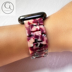 Puede incluir: Una correa de reloj con un patrón de mármol rosa, blanco y negro. La correa está hecha de un material plástico duro y tiene un diseño elegante y moderno.