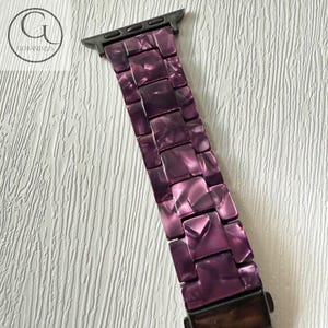 May include: A watch band featuring a purple marbled resin link design with a dark metal connector at the top. The links have a glossy finish with varying shades of deep violet and lighter purple tones, creating a textured appearance throughout.
