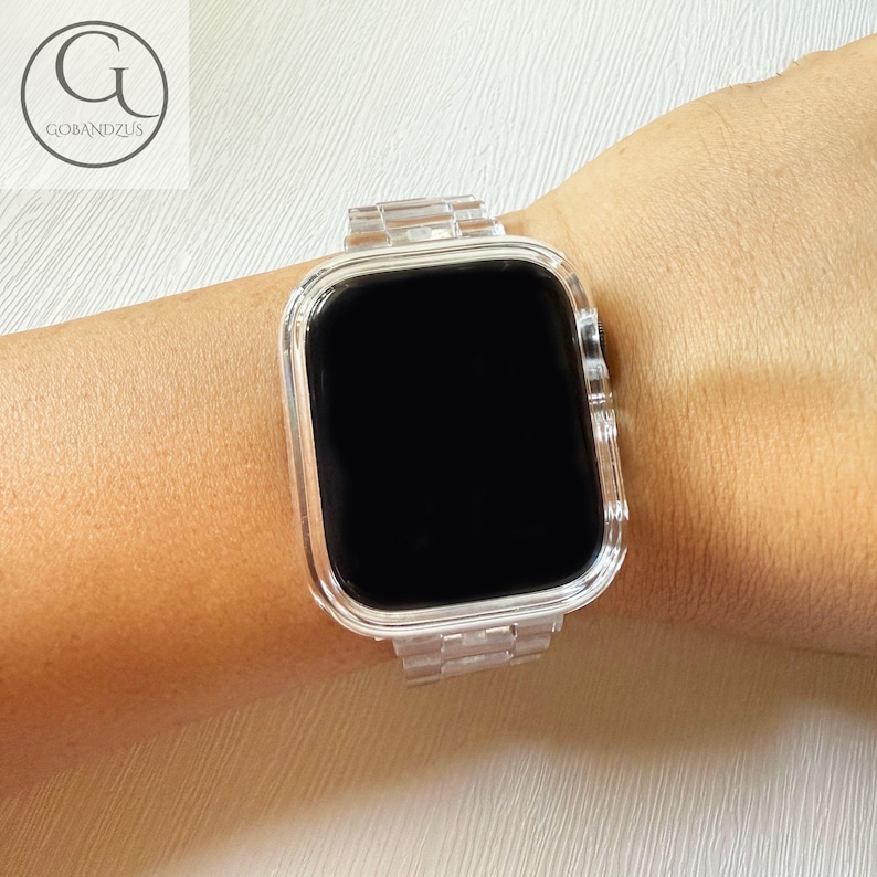 May include: A clear, transparent smartwatch band and protective case set featuring a link-style bracelet design. The watch face is black and rectangular with rounded corners, encased in a matching transparent frame that secures the device.