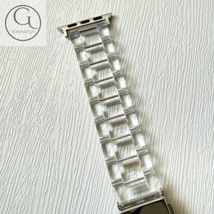 May include: A clear, transparent watch band featuring a linked, multi-segment design with a metallic silver-toned connector at the top. The band is constructed from smooth, rigid material and includes a secure metal clasp mechanism at the bottom end.