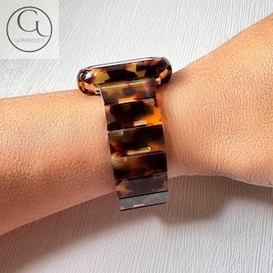 Könnte beinhalten: Ein braunes und schwarzes Schildpatt-Armband mit einer goldenen Schließe. Das Armband ist aus hartem Kunststoff gefertigt und hat eine glänzende Oberfläche.