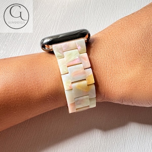 May include: A white and pink Apple Watch band with a shell-like pattern. The band is made of a durable material and has a classic design.