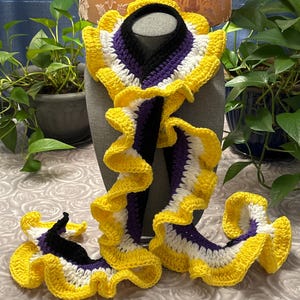 May include: A handmade, crochet scarf in the non-binary pride flag colors: yellow, white, purple, and black. The scarf has a ruffled edge and is displayed on a mannequin head. The scarf is a unique accessory.