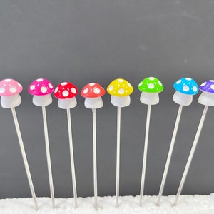 May include: A set of eight miniature mushroom garden stakes. The mushrooms are made of plastic and have white polka dots. The colors of the mushrooms are pink, red, orange, yellow, green, blue, purple, and light blue.