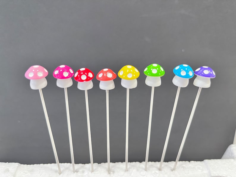 May include: A set of eight miniature mushroom garden stakes. The mushrooms are made of plastic and have white polka dots. The colors of the mushrooms are pink, red, orange, yellow, green, blue, purple, and light blue.