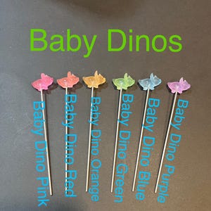 May include: Six colorful baby dinosaur figurines on sticks. The dinosaurs are pink, red, orange, green, blue, and purple.