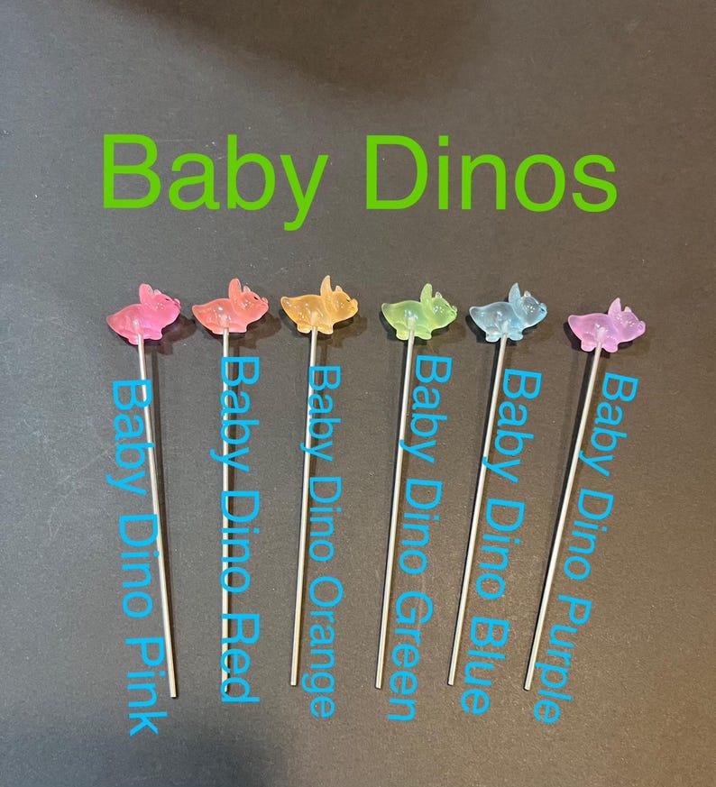 May include: Six colorful baby dinosaur figurines on sticks. The dinosaurs are pink, red, orange, green, blue, and purple.