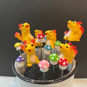 May include: A white ceramic mug with a black rim holds a collection of colorful mushroom-shaped picks with yellow dragon figurines on top.