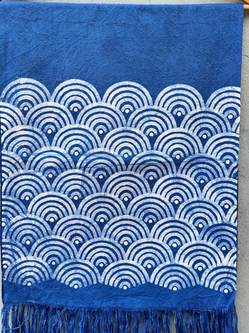 K&ouml;nnte beinhalten: Blaues Textil mit wei&szlig;em Wellenmuster. Das Design zeigt sich wiederholende Halbkreise, die einen geschichteten Effekt erzeugen. Der untere Rand hat Fransen. Der Stoff ist tiefblau.