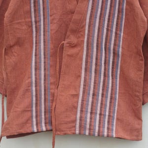 Puede incluir: Una blusa estilo kimono de color &oacute;xido con mangas cortas. La parte delantera presenta rayas verticales en tonos morado, blanco y gris. La blusa tiene cierres de lazo y est&aacute; hecha de una tela suave y texturizada.