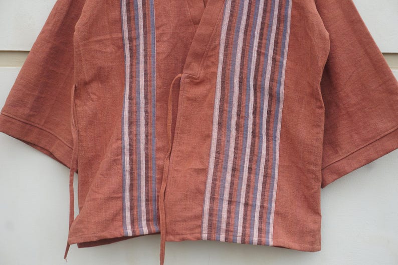 Puede incluir: Una blusa estilo kimono de color &oacute;xido con mangas cortas. La parte delantera presenta rayas verticales en tonos morado, blanco y gris. La blusa tiene cierres de lazo y est&aacute; hecha de una tela suave y texturizada.