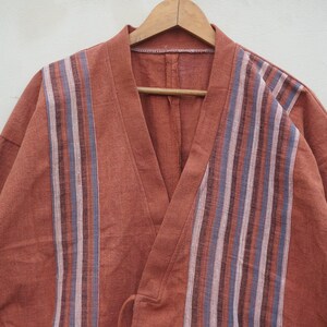 Puede incluir: Bata estilo kimono de color &oacute;xido con un dise&ntilde;o a rayas en la parte delantera. La bata est&aacute; hecha de una tela suave y cuelga de una percha de madera. Las rayas son en tonos de azul, morado y blanco.