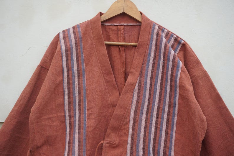 Puede incluir: Bata estilo kimono de color &oacute;xido con un dise&ntilde;o a rayas en la parte delantera. La bata est&aacute; hecha de una tela suave y cuelga de una percha de madera. Las rayas son en tonos de azul, morado y blanco.