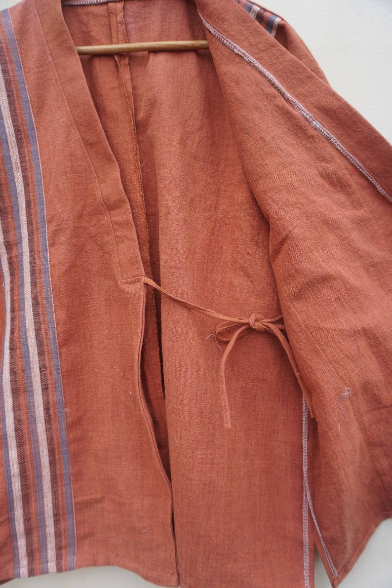 Puede incluir: Chaqueta abierta de color &oacute;xido con un acento a rayas en el lado izquierdo. Las rayas incluyen tonos de blanco, rosa y azul. La chaqueta tiene un cierre de lazo en la cintura y est&aacute; hecha de una tela texturizada.