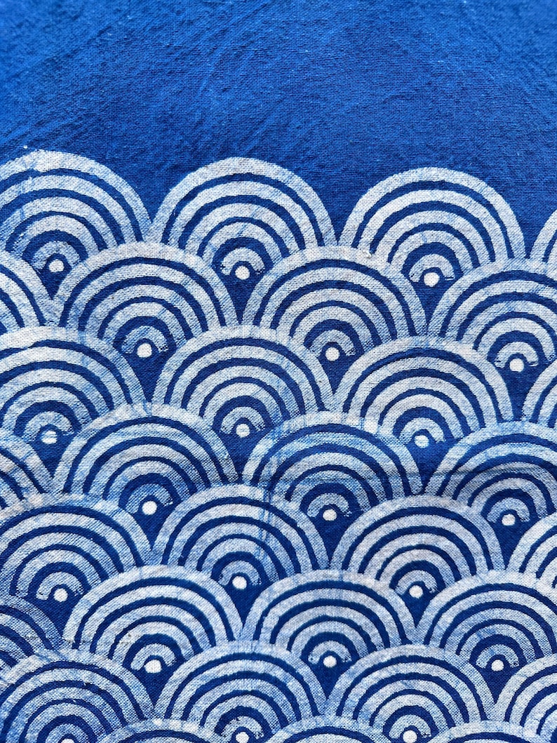 K&ouml;nnte beinhalten: Nahaufnahme eines blauen Stoffes mit einem sich wiederholenden Muster aus wei&szlig;en, konzentrischen Halbkreisen. Das Design erinnert an stilisierte Wellen oder B&ouml;gen und erzeugt einen strukturierten, geschichteten Effekt. Der Hintergrund ist einfarbig, tiefblau.
