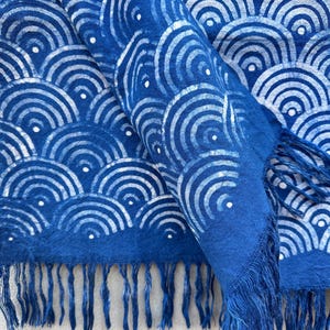 K&ouml;nnte beinhalten: Blauer Schal mit wei&szlig;em Wellenmuster und Fransen. Der Schal besteht aus einem weichen Stoff und hat ein sich wiederholendes Design aus wei&szlig;en Halbkreisen mit kleinen wei&szlig;en Punkten. Die Fransen sind in einem dunkleren Blauton gehalten.