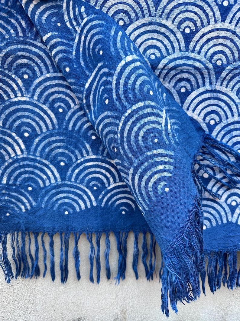 K&ouml;nnte beinhalten: Blauer Schal mit wei&szlig;em Wellenmuster und Fransen. Der Schal besteht aus einem weichen Stoff und hat ein sich wiederholendes Design aus wei&szlig;en Halbkreisen mit kleinen wei&szlig;en Punkten. Die Fransen sind in einem dunkleren Blauton gehalten.