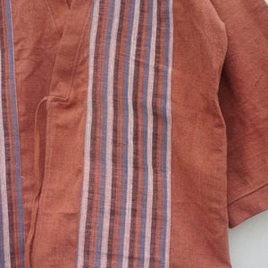 Puede incluir: Prenda de color &oacute;xido, de manga corta, con detalles de rayas verticales en tonos rosa, azul y marr&oacute;n. La tela parece ser un material suave y tejido. La prenda tiene un dise&ntilde;o envolvente.