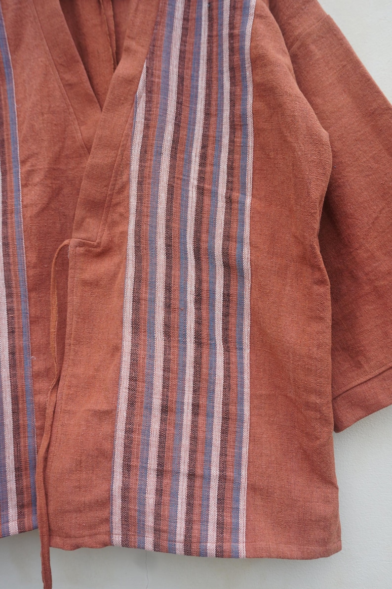 Puede incluir: Prenda de color &oacute;xido, de manga corta, con detalles de rayas verticales en tonos rosa, azul y marr&oacute;n. La tela parece ser un material suave y tejido. La prenda tiene un dise&ntilde;o envolvente.