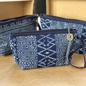 Peut inclure: Trois pochettes à fermeture éclair à motifs bleus et blancs. Les pochettes ont une forme rectangulaire avec une fermeture éclair et une garniture bleu foncé. Une pochette a une petite pièce d'or et une gland attachés à la fermeture éclair. Le tissu a un motif géométrique.