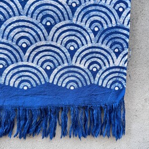 K&ouml;nnte beinhalten: Blau-wei&szlig; gemusterter Stoff mit einem wellenartigen Design. Der Stoff hat einen dunkelblauen Rand mit Fransen am unteren Rand. Das Muster ist eine sich wiederholende Reihe von Halbkreisen.