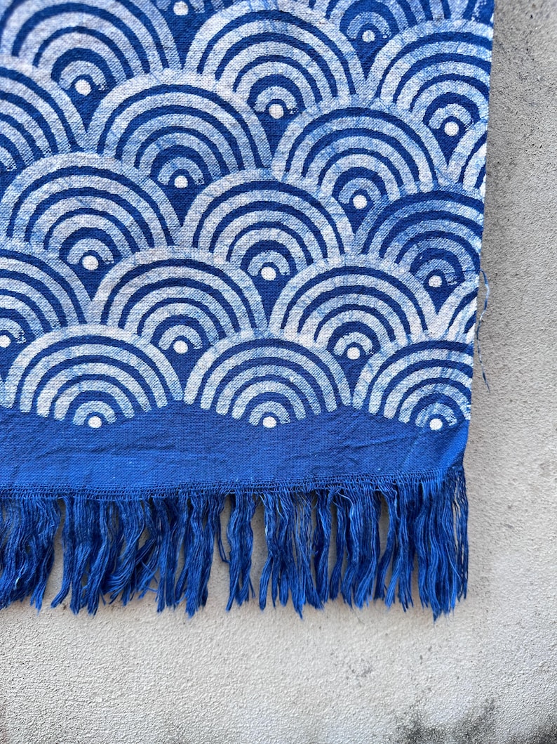 K&ouml;nnte beinhalten: Blau-wei&szlig; gemusterter Stoff mit einem wellenartigen Design. Der Stoff hat einen dunkelblauen Rand mit Fransen am unteren Rand. Das Muster ist eine sich wiederholende Reihe von Halbkreisen.