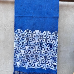 K&ouml;nnte beinhalten: Ein leuchtend blaues Textil mit wei&szlig;em Wellenmuster und Fransen. Der Stoff ist ein tiefes Blau mit einem sich wiederholenden Design aus wei&szlig;en, halbkreisf&ouml;rmigen Wellen. Der untere Rand hat Fransen.