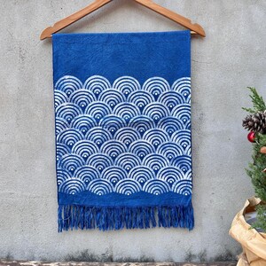K&ouml;nnte beinhalten: Blauer Stoff mit wei&szlig;em Wellenmuster, an einem Holzb&uuml;gel aufgeh&auml;ngt. Der untere Rand hat Fransen. Im Hintergrund ist ein kleiner Weihnachtsbaum zu sehen.