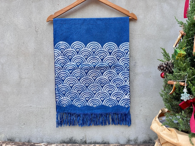 K&ouml;nnte beinhalten: Blauer Stoff mit wei&szlig;em Wellenmuster, an einem Holzb&uuml;gel aufgeh&auml;ngt. Der untere Rand hat Fransen. Im Hintergrund ist ein kleiner Weihnachtsbaum zu sehen.