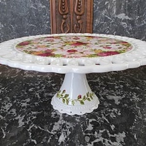 May include: White cake stand with a scalloped edge and a floral design. The stand has a pedestal base with a floral design.