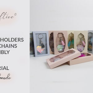 May include: A collection of small, clear boxes with keychains inside. Each box has a different color and features a different word, such as "Believe", "Hope", and "Love". The boxes are arranged in a row on a white surface. The text "Boxes and Holders for Keychains Assembly" is visible in the image.