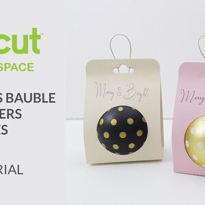 Op de afbeelding: Twee kerstversieringhouders, een beige en een roze, met een gouden en zwarte stippenversiering in de beige houder en een gouden en witte stippenversiering in de roze houder. De houders hebben een uitsparing voor de versiering en een ophanglus bovenaan. De beige houder heeft de tekst "Merry & Bright" en de roze houder heeft de tekst "Merry Christmas!"