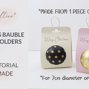 Op de afbeelding: Twee kerstbalhouders gemaakt van &eacute;&eacute;n stuk papier. De houders zijn beige en roze en hebben een uitsparing voor een kerstbal van 7 cm doorsnee. De beige houder heeft de tekst "Merry Christmas!" en de roze houder heeft de tekst "Merry & Bright".