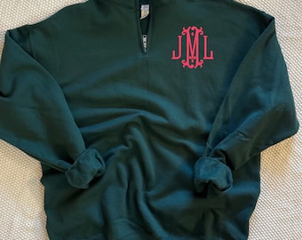 May include: A dark forest green quarter-zip sweatshirt featuring a stand-up collar and a silver-toned metal zipper. On the upper left chest, there is an embroidered monogram in bright pink thread displaying the letters J, M, and L.