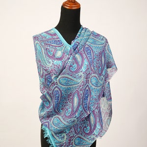 May include: A blue paisley patterned scarf with a fringed edge. The scarf is draped over a wooden mannequin.