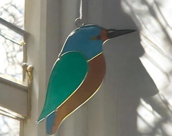 Op de afbeelding: Een vogel ornament van gekleurd glas met blauwe, groene en bruine kleuren. De vogel hangt aan een wit touwtje.