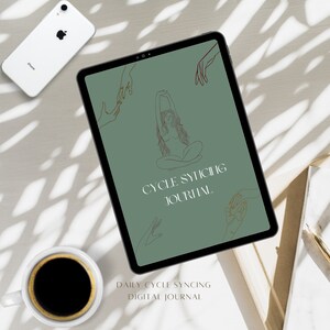 以下が含まれることがあります： 「Cycle Syncing Journal」のテキストが入ったタブレット。タブレットの周りには白いiPhone、コーヒーカップ、ノートが置かれています。ジャーナルは、女性と手の線画が描かれた緑色の背景です。