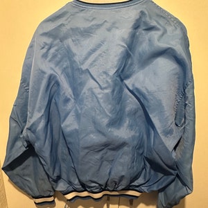 K&ouml;nnte beinhalten: Eine hellblaue Bomberjacke mit wei&szlig;en und dunkelblauen Rippb&uuml;ndchen an Kragen, &Auml;rmelb&uuml;ndchen und Saum.
